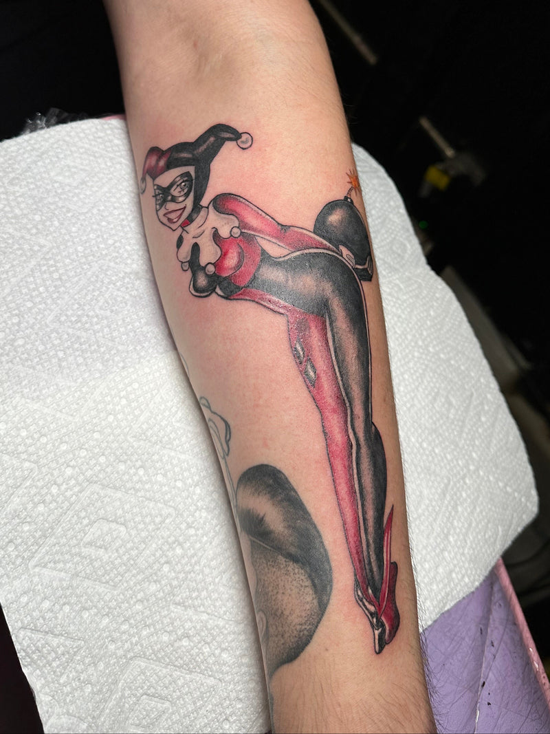 Tattoo of a harley quinn on a person's arm, with a white paper towel underneath.