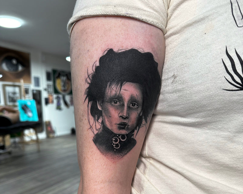Person with a tattoo of a woman's face on their arm, standing indoors.